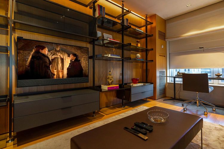 Modern media room with wooden shelving, flat-screen television, and a desk chair by the window
