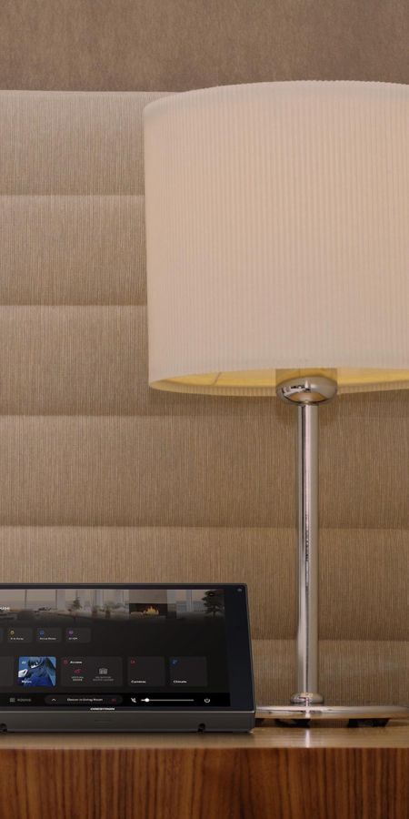Smart home control interface displaying menus next to a lit table lamp on a wooden nightstand