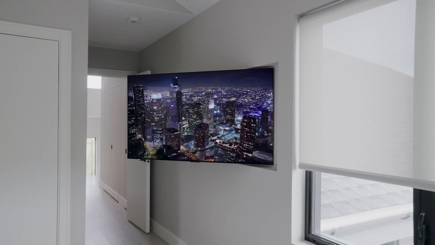 Flat-screen television displaying a city night skyline mounted on a neutral hallway wall