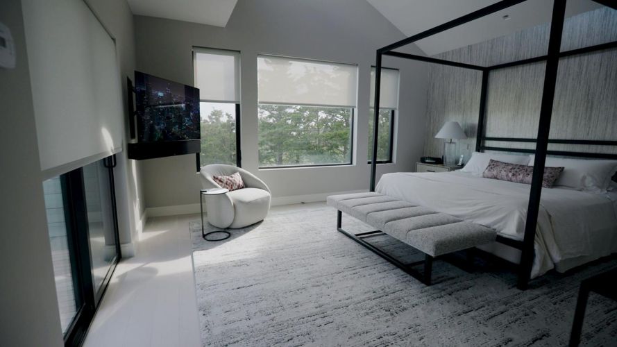Contemporary bedroom with a black canopy bed, white bedding, a grey rug, and large windows