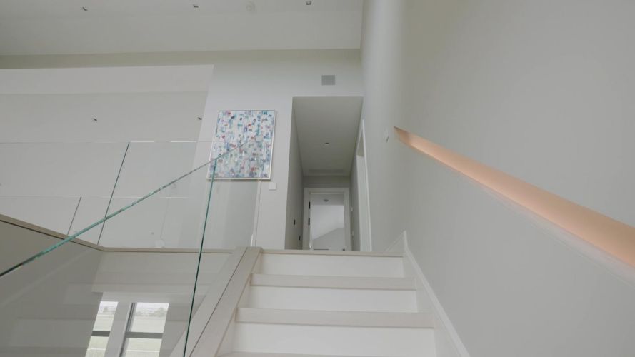 Low-angle view looking up a white contemporary staircase with glass panels and a recessed light