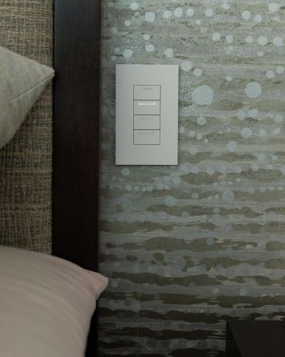 Smart home control panel mounted on green textured wallpaper next to a dark wood headboard