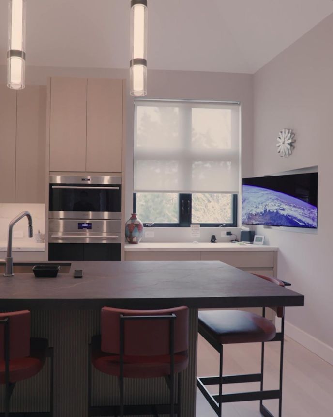 Modern kitchen with a dark marble island, red barstools, and wall-mounted television screen