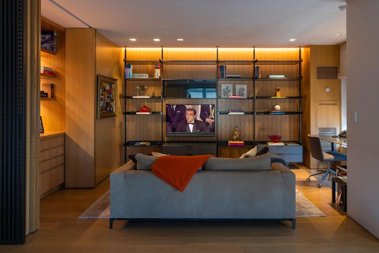 Grey sofa with an orange throw blanket facing a built-in wooden entertainment center with a TV