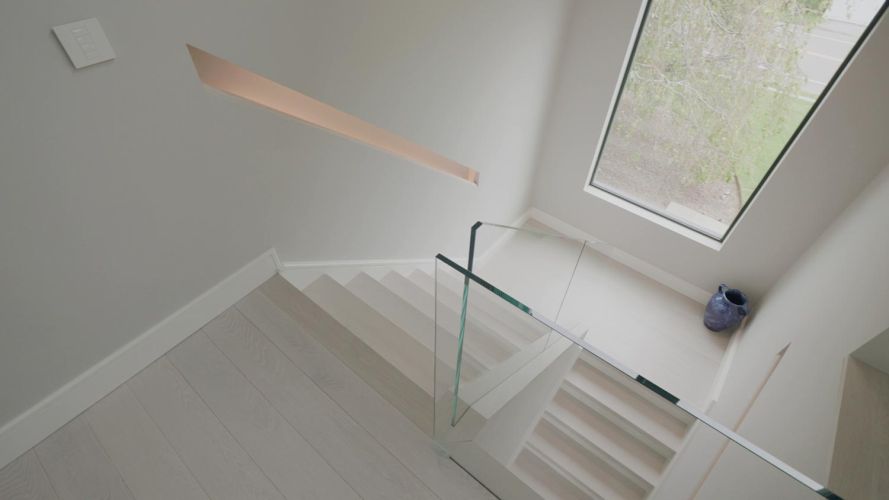 High-angle view of a white modern staircase with clear glass railings and a large window