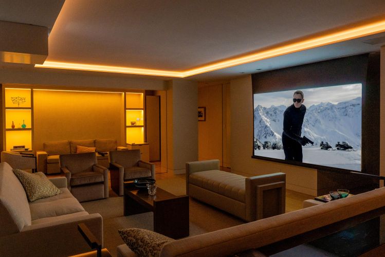 Home theater room with warm cove lighting, plush seating, and a movie playing on a large screen