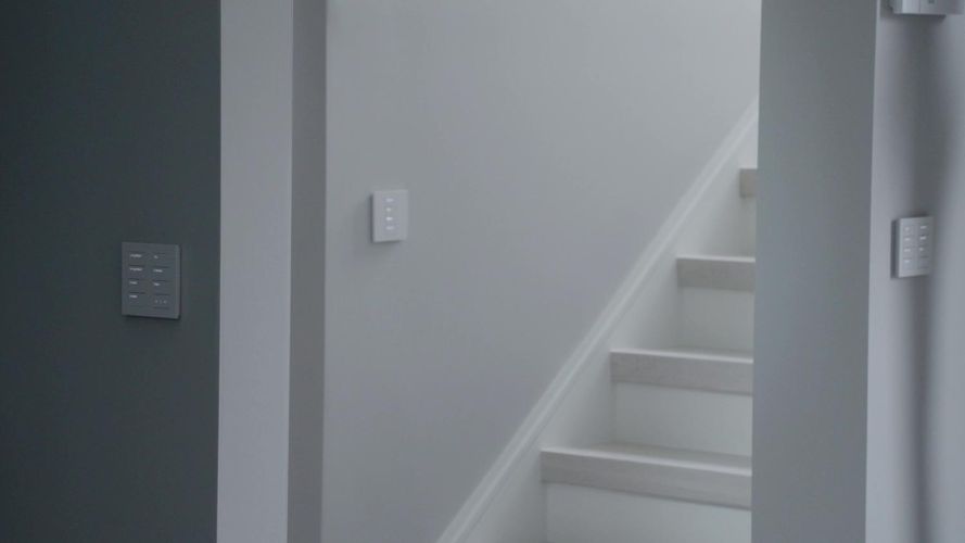 Dark grey and white walls featuring modern multi-button smart keypads near a white staircase