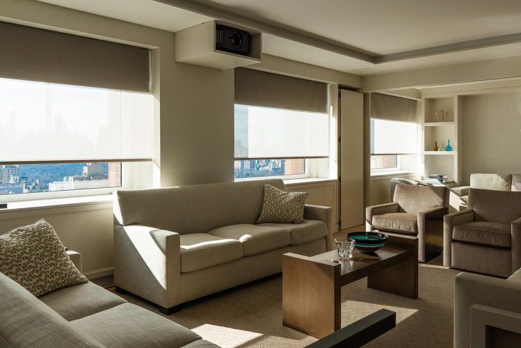 Bright contemporary living room with beige sofas, coffee table, and large shaded windows