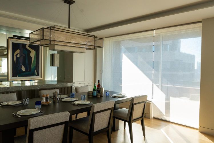 Modern dining room with large rectangular chandelier, dark wood table, and window shades