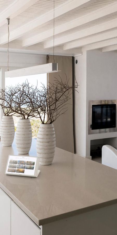 Smart home control tablet resting on a neutral kitchen island with large branch centerpieces