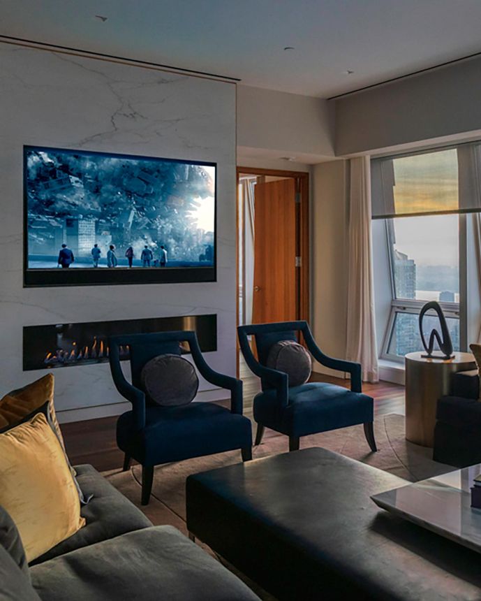 Luxury high-rise living room featuring two blue armchairs, a fireplace, and city views