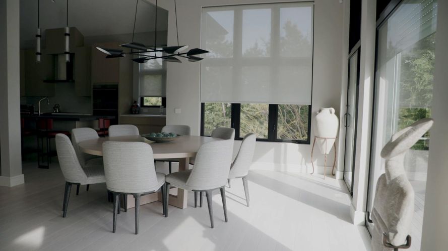 Modern dining room with a round wooden table, grey upholstered chairs, and a minimalist chandelier