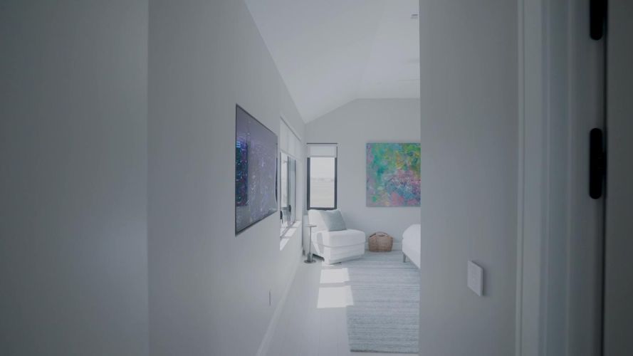 Bright hallway with a wall-mounted television leading into a modern bedroom with colorful art