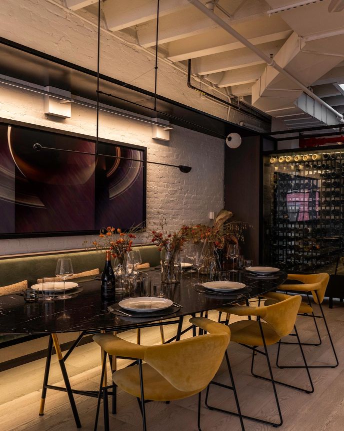 Chic dining room with a long black marble table, yellow velvet chairs, and a glass wine cellar