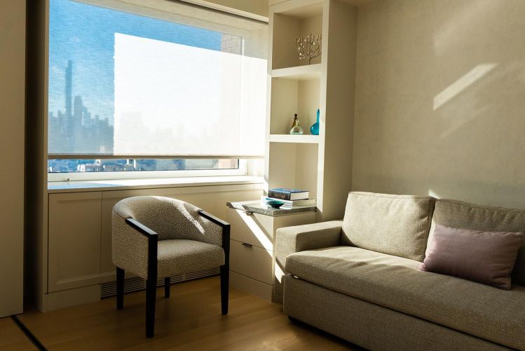 Sitting area with patterned armchair, beige sofa, and built-in shelving next to a window