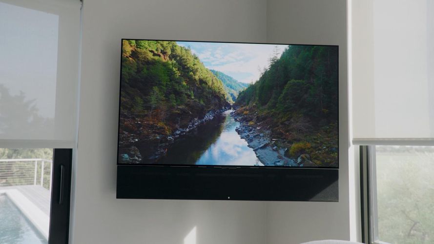 Television displaying a scenic river landscape mounted on a wall between two windows
