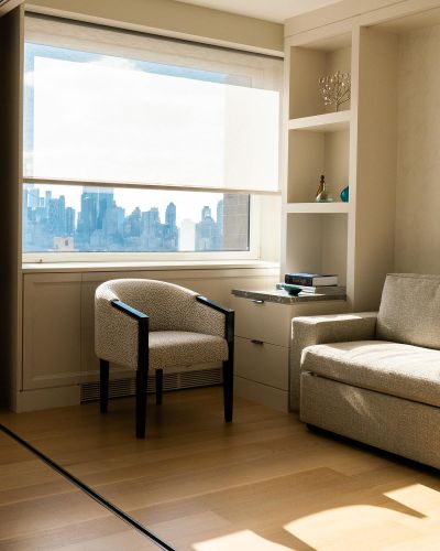 Sunlit corner reading nook with an armchair, sofa, and city skyline view through the window