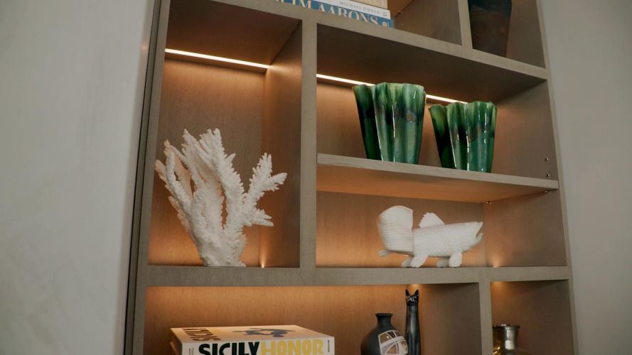 Built-in shelving units with integrated warm lighting displaying white coral and green glassware