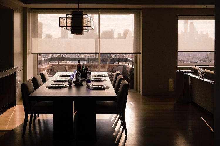 Silhouette view of a set dining table under a geometric chandelier facing a balcony window