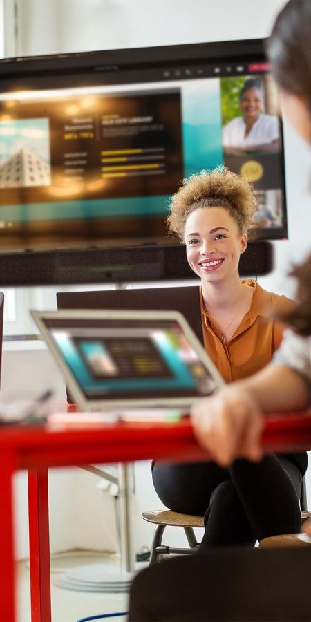 Smiling woman in an orange top working on a laptop during a modern conference room meeting