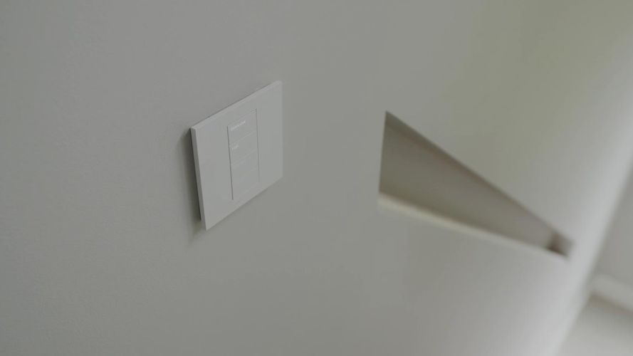 White multi-button smart keypad controller mounted on a light grey wall next to a staircase