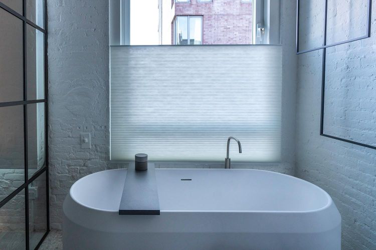 White freestanding bathtub under a large window with a white privacy shade