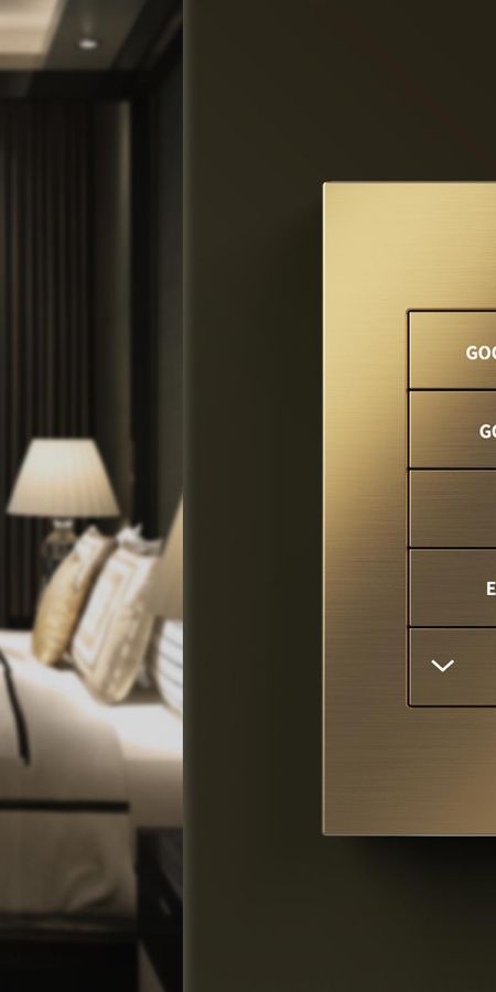 Close-up of a brushed gold wall keypad with lighting scene buttons next to a blurred bedroom